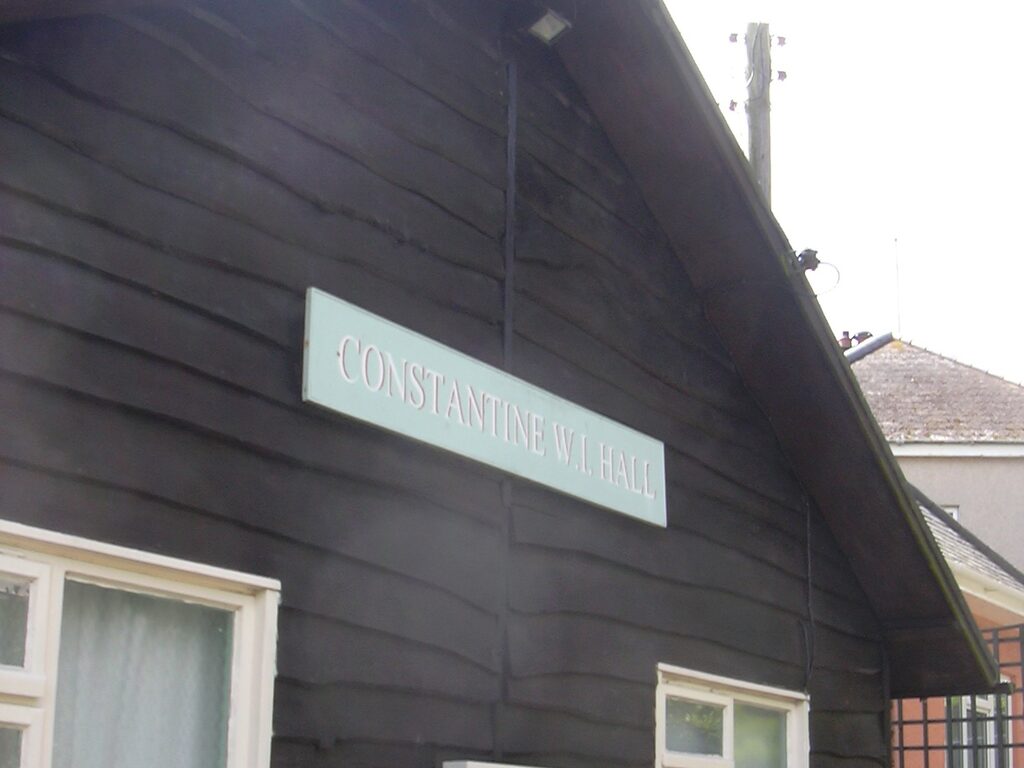 The painted sign reading Constantine W.I. Hall on the dark timber side of the village hall